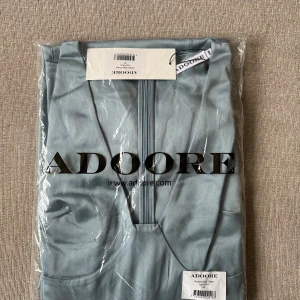 Ljusblå långklänning från Adoore - Säljer en elegant ljusblå Andora Maxi Dress från Adoore. Klänningen har en v-ringad hals, långa puffärmar och figurnära passform med markerad midja. Materialet har en satinliknande finish som ger en lyxig känsla. Perfekt för dig som vill sticka ut med stil. Den är helt oanvänd med orginalfärpackning kvar 🩵