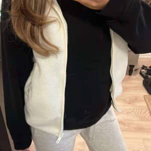 Vit fleeceväst med dragkedja - Säljer en vit fleeceväst med dragkedja framtill och praktiska fickor på sidorna. Perfekt att slänga över hoodien för extra värme eller ha över en topp i skolan 🌟