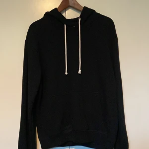 Svart hoodie från Pier One - Svart hoodie från Pier One med klassisk design. Tröjan har huva med vita snören och en stor magficka framtill. Långärmad och i mjukt material som passar perfekt för chill dagar. Enkel och stilren look som funkar till det mesta. Storlek medium men passar även klockrent för S