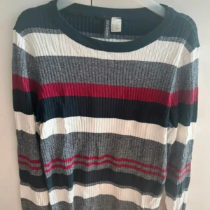 Randig ribbad tröja från H&M - Säljer en randig ribbad tröja från H&M i färgerna grå, vit, röd och mörkblå. Tröjan har lång ärm och rund halsringning, perfekt för dig som gillar en färgglad och bekväm stil
