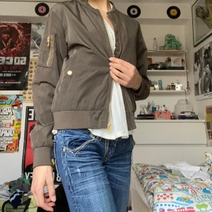 Bomberjacka  - Snygg khakifärgad bomberjacka från Denim Factory med guldfärgade dragkedjor och knappar. Jackan har ribbade muddar, fickor med knappstängning och en extra ficka på ärmen. 