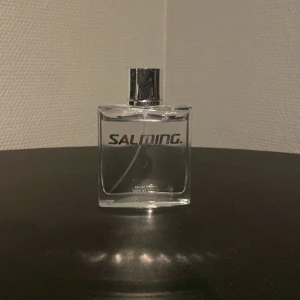 Salming Eau de Toilette 100ml - Fräsch och sportig parfym från Salming i en stilren, transparent glasflaska med silvrig kork. Flaskan rymmer 100 ml eau de toilette och har en modern, fyrkantig design med tydlig logga framtill. Perfekt för dig som gillar en clean och energisk doft.