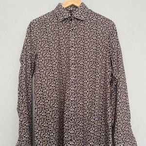 Mönstrad skjorta från Venti, body fit - Säljer en slim mad skjorta från Venti med brunt, grått och svart cirkelmönster. Skjortan har lång ärm, klassisk krage och knäppning framtill. Perfekt för dig som gillar unika prints och en tajtare passform.