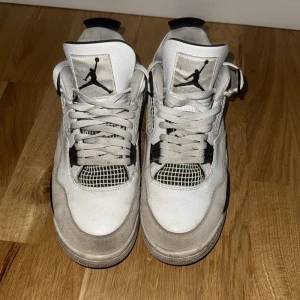 Nike Air Jordan 4 Retro vit/svart - Säljer ett par Nike Air Jordan 4 Retro i vitt och svart med klassisk meshpanel, skinn och mockadetaljer som är sparsamt använda. Ikonisk Jumpman-logga på plös och häl, samt coola plastdetaljer och snörning. Perfekta för dig som vill sticka ut med en tidlös sneaker.