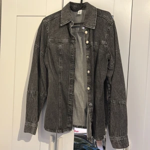 Svart jeansjacka från &Denim, S - Säljer en svart tvättad jeansjacka från &Denim i storlek S. Jackan har klassisk krage, synliga sömmar och silverfärgade knappar framtill. Långärmad modell i denim med en cool, lite sliten look. Perfekt för dig som gillar streetstyle.