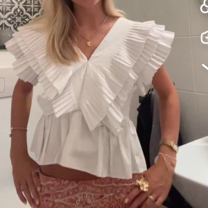 Vit blus med volangkrage - Superfin vit blus med djup v-ringning och stora, plisserade volangdetaljer över axlar och bröst. Blusen har en luftig passform och är tillverkad i bomull, vilket gör den perfekt för vår och sommar. Den unika volangkragen ger en trendig och cool look. skicket är som på bilderna. Ej tvättad då jag ej vill att vikningen ska gå bort, men det går säkert bort i tvätten om man vill tvätta
