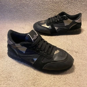 Valentino Garavani svarta sneakers - Snygga svarta Valentino Garavani sneakers med coolt kamouflagemönster i grått och silverdetaljer på sulan där bak 