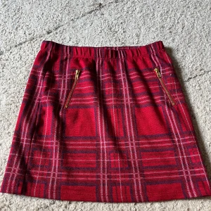 Rutig röd tajt kjol  -  rutig tajt kjol från Holly & Whyte by Lindex i rött med inslag av mörkblått och vitt. Kjolen har två guldfärgade dragkedjor framtill 