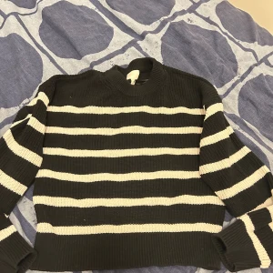 Randig stickad tröja från H&M - Säljer en svart och vit randig stickad tröja från H&M i storlek S. Tröjan har en klassisk rund halsringning och långa ärmar. Perfekt för dig som gillar en chill och stilren look med lite edge.