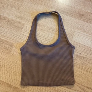 Brun ribbad linnetopp XS - Säljer en brun ribbad linnetopp i storlek XS. Toppen är ärmlös med rund halsringning och croppad passform, perfekt till jeans eller kjol. Materialet är mjukt och stretchigt för en bekväm känsla hela dagen.