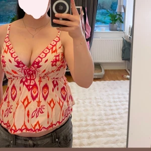 Mönstrad linnetopp med korsade band - Säljer en linnetopp med färgstarkt mönster i rosa/röd och orange. Toppen har smala axelband som korsas i ryggen och en djup v-ringning framtill. Funkar i både storlek M och S💗 