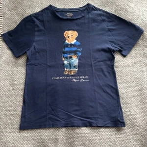 Blå t-shirt med Polo Bear från Ralph Lauren - Säljer en snygg blå t-shirt från Ralph Lauren med det ikoniska Polo Bear-motivet på framsidan. T-shirten är kortärmad och tillverkad i mjuk bomull. Använd ett väldigt fåtal gånger. |nypris:695|Storlek S|🐻💙