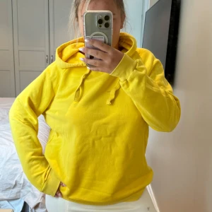 Gul hoodie från Gina Tricot - Super gul hoodie från Gina Tricot i storlek L. Tröjan har huva med snörning och är tillverkad i mjuk bomullsmix. Perfekt för dig som vill sticka ut med en färgglad och bekväm stil. Långärmad och loose fit. Har en fläck framtill som jag inte fått bort men inte kämpat så mycket med de heller