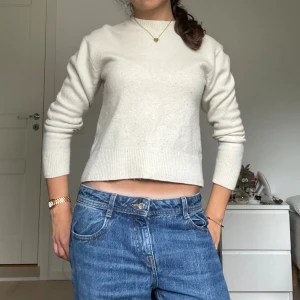 Vit stickad ulltröja med croppad passform - Säljer en stilren vit stickad tröja med croppad passform i ull!!. Tröjan har rund halsringning, långa ärmar och breda ribbade muddar vid ärmslut och nederkant. Liiite nopprig men det går att ta bort lätt eftersom det är ull! 