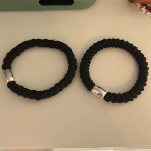 Knekki - Två coola svarta armband med flätad design och snygga silverfärgade detaljer. Perfekt att bära tillsammans eller var för sig för en enkel men stilren look. Passar dig som gillar minimalistiska accessoarer med en twist.