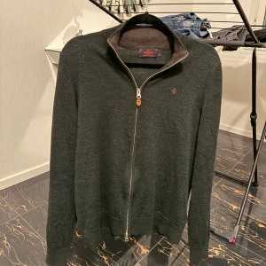 Mörkgrön merinoullskofta från Morris - Snygg mörkgrön kofta från Morris i 100% merinoull. Modellen har hel dragkedja framtill, ståkrage och diskret broderad logga på bröstet. Perfekt för lager-på-lager och passar till det mesta. Klassisk och stilren design.  (finns ett litet hål bakom höger arm) 