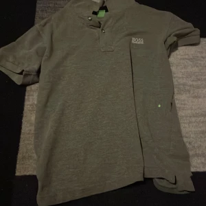 Grå kortärmad t-shirt från Hugo Boss - Snygg grå t-shirt från Hugo Boss med korta ärmar och klassisk krage. T-shirten har broderad logga på bröstet och är tillverkad i mjuk bomull. Perfekt för en clean och stilren look.