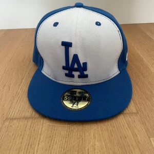 Blå och vit LA Dodgers keps New Era - Snygg LA Dodgers keps från New Era 59FIFTY-serien. Kepsen är blå med vit frontpanel och blått LA-broderi framtill. Klassisk rak skärm och broderade ventilationshål. MLB-logga baktill och New Era-logga på sidan. Perfekt för dig som gillar sportig streetstyle.