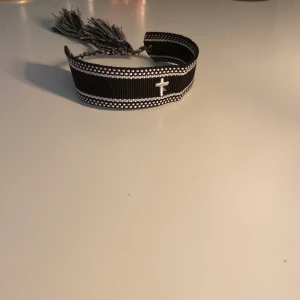 Svart och vitt tygarmband med kors som är hemmagjort!!! - Snyggt svart armband i tyg med vita detaljer och ett broderat kors i mitten. Jag har gjort det ensam hemma!! Med lite hjälp från min mamma… Säljer ett för 110kr och två för 160kr!!! Skriv för mer frågor!🙂