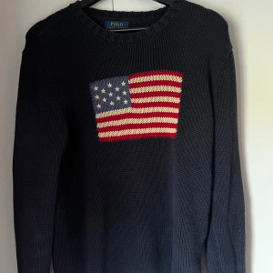 Mörkblå stickad tröja Polo Ralph Lauren - Mörkblå stickad tröja från Polo Ralph Lauren med amerikansk flagga broderad på bröstet. Tröjan har rund halsringning och långa ärmar. Står XL men är i vuxen storlek men som vanlig är den M. Priset är inte hugget i sten vid snabb affär.