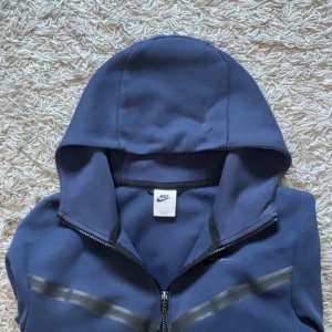 Blå hoodie från Nike med dragkedja - Nike hoodie i mörkblått med hel dragkedja och huva. Snygga svarta detaljer över bröstet och på ärmen. Storlek S passar även M.