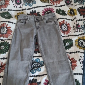 Grå raka jeansbyxor - Säljer ett par grå jeansbyxor med klassisk femficksmodell och raka ben. Byxorna har bälteshällor och dragkedja med knapp framtill. Perfekta för dig som gillar en enkel och stilren look.