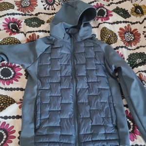 Blå cardigan - Snygg blå pufferjacka med quiltat mönster på framsidan och släta ärmar. Jackan har huva och dragkedja framtill, perfekt för kyliga dagar. Sportig look och skön passform.