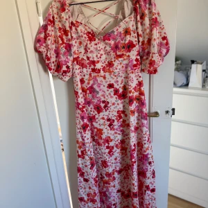 Blommig långklänning från Missay - Superfin långklänning från Missay med blommigt mönster i rosa, rött och orange på vit botten. Klänningen är i storlek M och har puffiga korta ärmar, snörning i ryggen och v-ringad hals. Den är oanvänd och har prislappen kvar!🥰