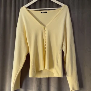 Ljusgul kofta från Gina Tricot - Superfin ljusgul kofta från Gina Tricot med v-ringning och dekorativa knappar framtill. Koftan har lång ärm och är gjord i ett mjukt material som känns skönt mot huden. Perfekt att slänga på sig när det är lite kyligt ute.