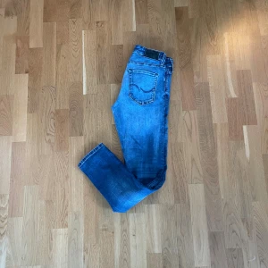 Jack and Jones Jeans - Snygga blå jeansbyxor i slim fit med klassisk femficksdesign och diskreta slitningar. Byxorna har normal midja och raka ben, perfekta för en avslappnad stil. Tillverkade i mjukt och slitstarkt bomullsmaterial. Passar dig som gillar en modern och enkel look.