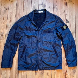 Stone Island vindjacka -   🧥 Stone Island Vindjacka Säljer en snygg och lätt blå vindjacka från Stone Island. Klassisk design med avtagbart kompassmärke på armen, logoknappar och praktiska fickor. Jackan är tillverkad i 84% polyamid och 16% polyester, vilket gör den både slitstark och bekväm.  ✅ Äkta – har Certilogo-tag för verifiering (se bild) 📍 Tillverkad i Rumänien 📏 Storlek:M 🔹 Färg: Marinblå 🔹 Skick:Mycket bra, sparsamt använd,  💸 Pris: 3499 Priset kan diskuteras                          Nypris ligger på 7300