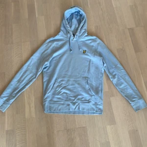 Ljusblå hoodie från Lyle & Scott - Helt ny ljusblå hoodie från Lyle & Scott med klassisk gul logga på bröstet. Tröjan har huva med snörning, magficka och långa ärmar med ribbade muddar. Perfekt för chill dagar och enkel att matcha med jeans eller joggers. Tveka inte på att fråga 🙋‍♂️