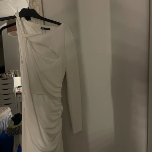 Vit  klänning från Zara - Säljer en ny vit, kort klänning från Zara med lång ärm på ena sidan och snygg cut-out detalj vid axeln.