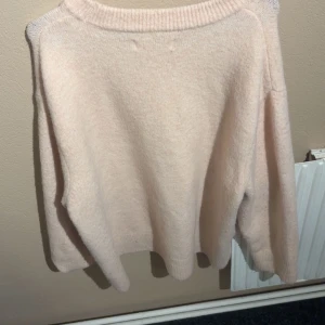 Ljusrosa stickad tröja med rund hals - Mysig ljusbeige stickad tröja med rund halsringning och långa ärmar. Tröjan har en avslappnad passform och ribbade muddar vid hals, ärmslut och nederkant. Perfekt för lager-på-lager under kyliga dagar.