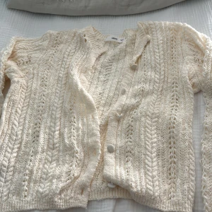 Beige stickad kofta från Mango - Säljer en beige stickad kofta från mango i storlek M. Koftan har ett öppet, luftigt mönster och stängs med knappar framtill. Perfekt för lager-på-lager och har långa ärmar samt ribbade muddar. Superfin till jeans eller klänning!