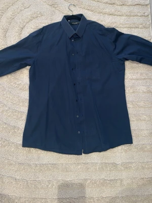 Mörkblå skjorta från Dolce & Gabbana - Snygg mörkblå skjorta från Dolce & Gabbana med klassisk krage och knappar hela vägen framtill. Skjortan har lång ärm och är gjord i mjuk bomull som känns skön mot huden. ORGINAL ( äkta )