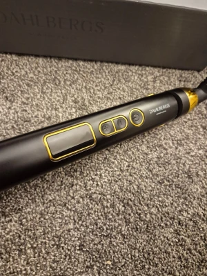 Dahlbergs plattång svart/guld - Oanvänd...Snygg plattång från Dahlbergs i svart med gulddetaljer och digital display. Ergonomisk design med smala plattor och praktiska knappar för temperaturkontroll. Perfekt för att styla håret och skapa släta eller vågiga looks. Kommer med lång sladd och låsfunktion.