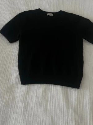 Svart stickad tröja från H&M - Svart stickad tröja från H&M med rund hals och korta ärmar. Enkel och stilren design som funkar till många olika looks. Mjuk och skön kvalitet, perfekt för dig som gillar minimalistiska plagg.