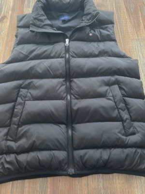 Svart dunväst från GANT - Säljer en svart dunväst från gant i storlek 158-164. Den är sparsamt använd och nästan i nyskick. Ny pris 1500kr