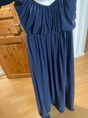 Marinblå långklänning axelbandslös - Säljer en marinblå långklänning med axelbandslös design och vackert draperad överdel. Klänningen har ett flytande fall och är gjord i ett lätt, mjukt material som ger en elegant siluett. Perfekt för dig som gillar stilrena och klassiska plagg. Perfekt för t.ex bal och fester osv klänningen ger push up priset går att diskutera 