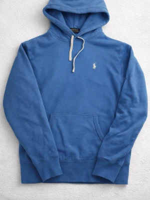 Blå hoodie från Polo Ralph Lauren  - Säljer en blå hoodie från Polo Ralph Lauren i storlek XS. Tröjan har huva med vit snörning, klassisk känguruficka och broderad logga på bröstet. Materialet är 60% bomull och 40% polyester, vilket gör den mjuk och skön. Perfekt för chill dagar.