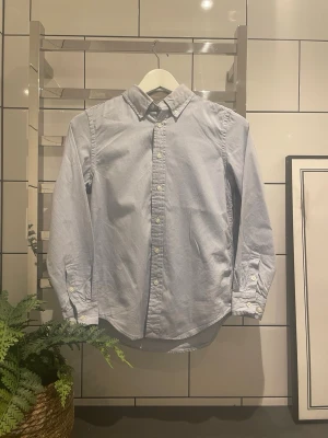 Ljusblå skjorta från Ralph Lauren - Klassisk ljusblå skjorta från Ralph Lauren med button-down krage och vita knappar framtill. Skjortan är långärmad och har en tidlös, clean look som passar till allt. Tillverkad i mjuk bomull för skön känsla hela dagen. Skjortan ser svårt märkbart urtvättad ut. Jag kan som vanligt alltid gå ner i pris + skriv vid minsta fråga ✨