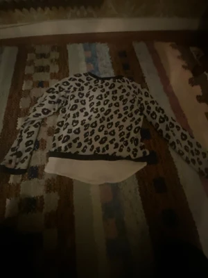Leopardmönstrad långärmad tröja - Säljer en cool långärmad tröja med leopardmönster i svart och grått. Tröjan har rund hals och en vit, längre nederdel som ger en lager-på-lager känsla. Perfekt för dig som gillar djurmönster och vill sticka ut lite extra.