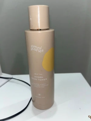Sunny Stories Hydra Body Toner - Hydra Body Toner från Sunny Stories är en brun utan sol-produkt i en beige plastflaska med gul detalj. Den ger en mjuk och naturlig solbrun ton till huden och är enkel att applicera. Perfekt för dig som vill ha en gradvis solkysst look.