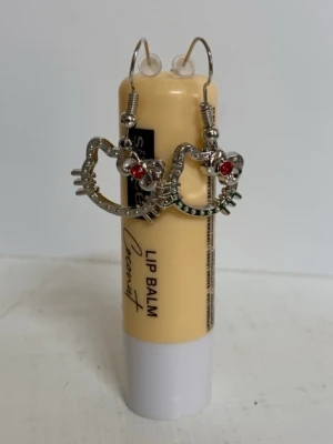 Hello Kitty örhängen i silverfärg - Säljer ett par snygga Hello Kitty örhängen i silverfärgad metall med röd detalj på rosetten. Örhängena har en öppen design med små nitar runt kanten och klassisk krok för enkel användning. Inte äkta silver!!