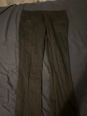 Svarta kostymbyxor med raka ben - Säljer ett par klassiska svarta kostymbyxor med raka ben och bälteshällor. Byxorna har en stilren look och passar perfekt till en snygg skjorta eller t-shirt. Materialet känns mjukt och har en lätt glans. Perfekta för dig som gillar en clean och enkel stil.