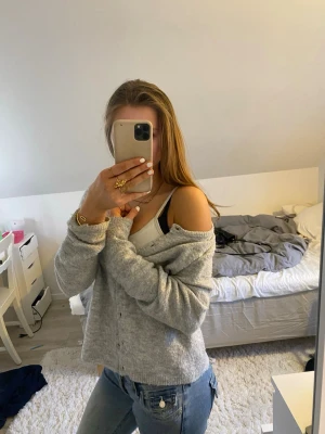 Grå stickad kofta från 157, XS - Mysig ljusgrå stickad kofta från 157 i storlek XS. Koftan har knappar framtill, lång ärm och en loose passform. Perfekt att slänga över ett linne eller t-shirt för en chill look.