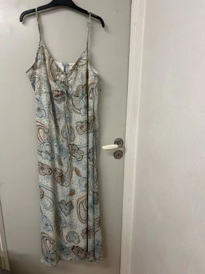  Vacker fallande klänning från ze-ze - Super fin fallande klänning som sitter så snyggt på. Den har en underklänning och därefter faller de snygga mönstret över!  Jätte snygga detaljer! Storlek L & använd en gång! Går att spänna in banden där bak som på en bh