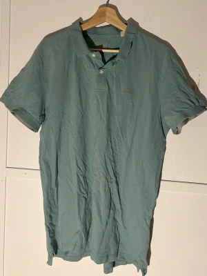 Grön pikétröja från Esprit - Säljer en stilren grön pikétröja från Esprit i ekologisk bomull. Tröjan har klassisk krage, korta ärmar och två knappar framtill. Perfekt till jeans eller shorts för en avslappnad look.