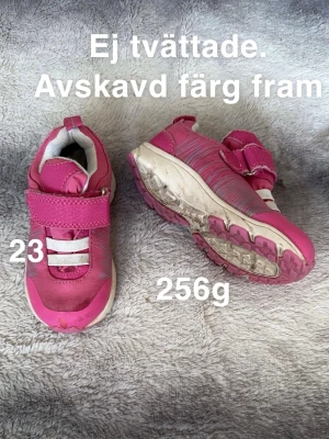 Rosa sneakers med kardborreband - Säljer ett par rosa sneakers med vita detaljer och praktiska kardborreband. Skorna har en rund tå och platt sula, perfekt för aktiva dagar. De har en sportig look med mönstrade inslag på ovansidan och är lätta att ta på och av.🌸 Avskavd färg. Ej tvättade. Storlek 23